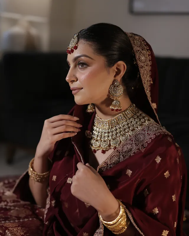 Bride in a maroon dupatta and gold jewellery, makeup by Samia